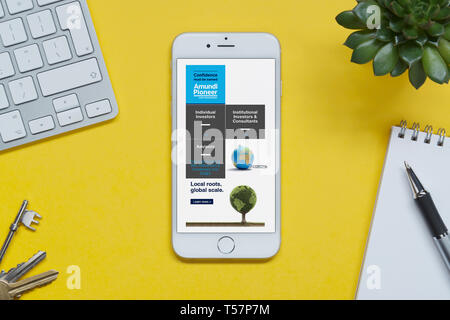 Un iPhone montrant l'Amundi Asset Management site web repose sur un fond jaune table avec un clavier, les touches, le bloc-notes et des plantes (usage éditorial uniquement) Banque D'Images