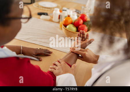 Femme dans les verres en mettant sa main sur la table pour l'infirmière pour mesurer le pouls Banque D'Images