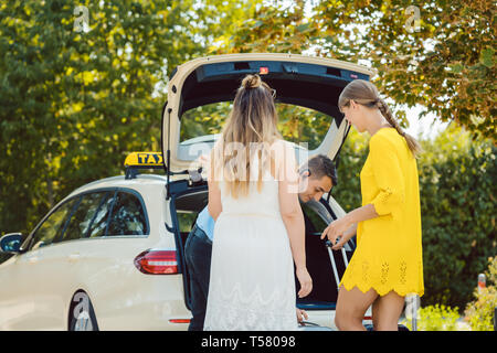 Chauffeur de taxi en mettant une assurance des femmes dans coffre de voiture Banque D'Images