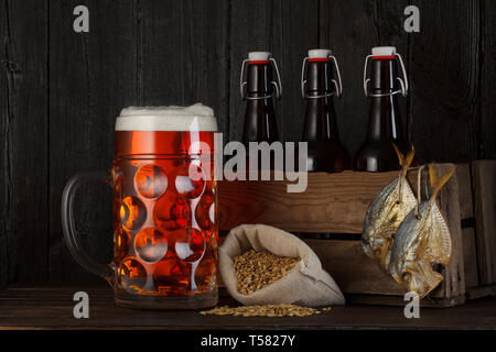 Verre de bière sur la table avec des caisses en bois plein de bouteilles, sac avec de l'orge de la bière et du poisson séché salé Banque D'Images