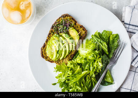 Toast à l'avocat avec du pesto, salade de choux et sur une assiette blanche et de glace café. Banque D'Images