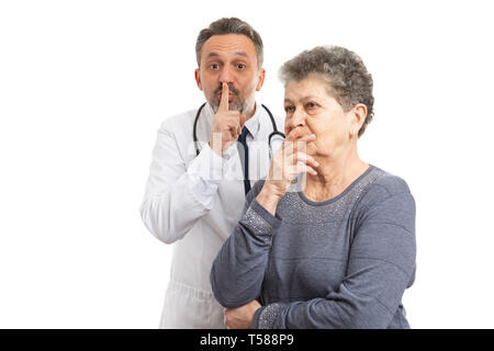 Médecin homme faire de geste chut en maintenant l'index derrière soupçonneux patient âgé isolé sur fond blanc Banque D'Images