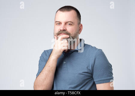 Bel homme en bleu chemise semble sérieusement à huis clos et frotte son menton Banque D'Images
