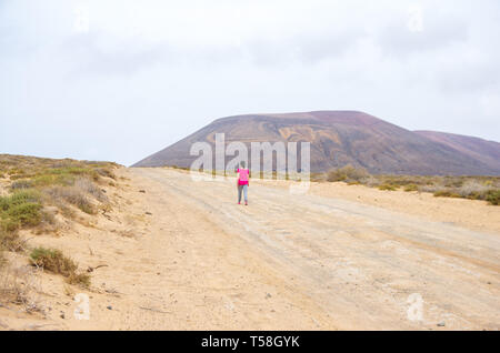 Woman in pink marchant sur un chemin de sable vers un volcan dans La Graciosa island Banque D'Images