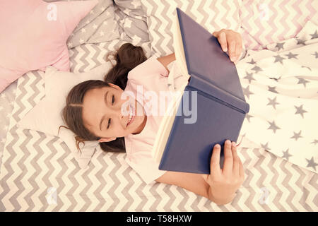 Lit enfant fille lay read book vue d'en haut. Encourager les habitudes utiles.Kid se préparer à aller au lit. Temps agréable dans une chambre confortable. Kid fille cheveux longs pyjamas mignons vous détendre et lire livre. Satisfait de professionnels. Banque D'Images