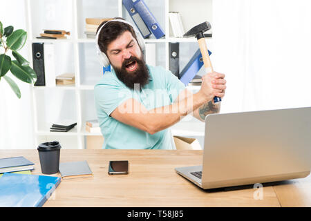 Logiciel obsolète. Décalage de l'ordinateur. Pour des raisons du retard de l'ordinateur. Comment fixer la traîne lente du système. La routine du bureau. Homme barbu bureau écouteurs swing marteau sur ordinateur. Connexion internet lente. Banque D'Images