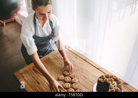Vue supérieure de femmes chef de pâtisserie préparation des cookies dans la cuisine. L'organisation des témoins sur baker femme grill avec un gâteau sur la table. Banque D'Images