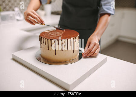 Chef pâtissier la préparation d'un gâteau dans la cuisine. Confiseur chocolat femelle répand le glaçage sur un gâteau. Banque D'Images