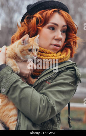 Portrait d'une jeune fille rousse avec un chat rouge en plein air, sur la rue Banque D'Images