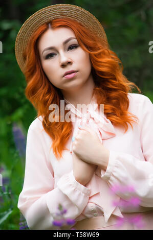 Une belle femme aux cheveux rouges et se pose dans un champ de lupins mauve et jouit de la vue dans le ressort Banque D'Images