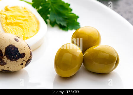 Oeufs de poulet bouilli avec des oeufs de cailles, d'olive et le persil sur la plaque blanche, des aliments sains Banque D'Images