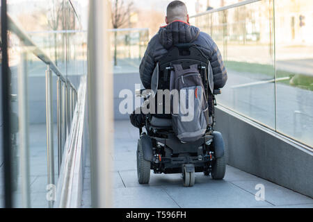 Homme dans un fauteuil roulant électrique à l'aide d'une rampe Banque D'Images