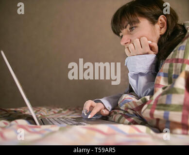 Jeune femme brune couchée sur le lit et travailler dans son ordinateur portable Banque D'Images