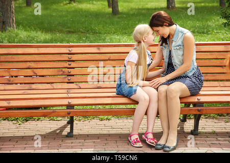 Maman et sa fille assise sur un banc dans un parc. La mère et l'enfant en famille. Banque D'Images