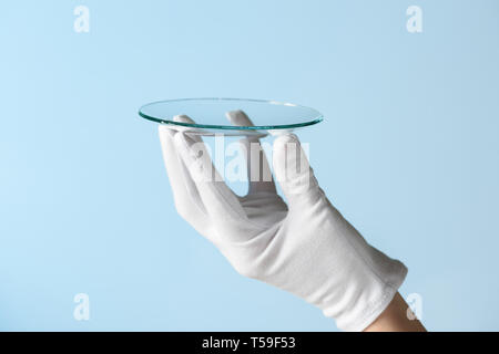 Nouvelles fonctionnalités de recherche de verre, hand in glove holding circle morceau de matériau transparent Banque D'Images