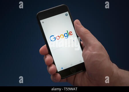 Un homme se penche sur son iPhone qui affiche le logo Google (usage éditorial uniquement). Banque D'Images