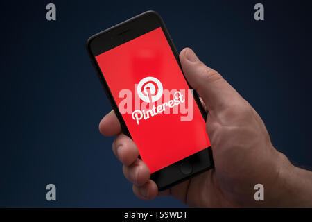 Un homme se penche sur son iPhone qui affiche le logo Pinterest (usage éditorial uniquement). Banque D'Images
