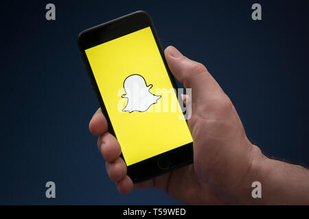 Un homme se penche sur son iPhone qui affiche le logo Snapchat (usage éditorial uniquement). Banque D'Images