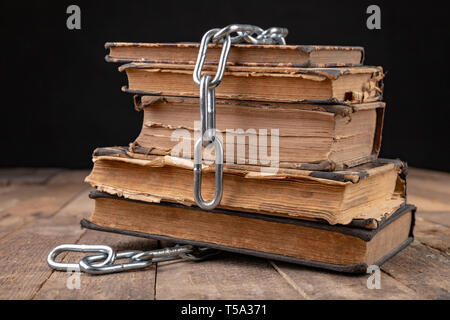 Livres anciens liés à une nouvelle chaîne brillante. Interdit old works artistes sur une table en bois. Fond sombre. Banque D'Images