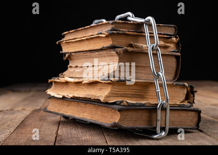 Livres anciens liés à une nouvelle chaîne brillante. Interdit old works artistes sur une table en bois. Fond sombre. Banque D'Images