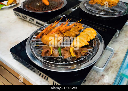 Différents types de kebabs sont frits sur un gril électrique dans la cuisine du restaurant de l'hôtel. La cuisson à la maison. Poêlée de crevettes, poulet, boeuf, porc frie Banque D'Images