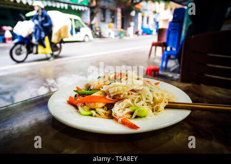 L'alimentation de rue d'Asie Thaïlande Vietnam. Une assiette de nouilles sur la table contre la rue asiatique avec les motos et les motards. Banque D'Images