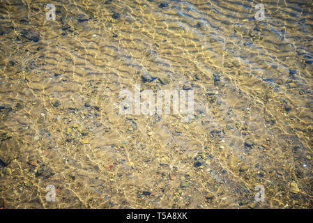 Arrière-plan de l'eau avec du jaune sable et galets sur le fond dans la lumière du soleil Banque D'Images
