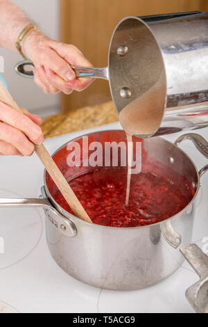 Woman pouring pectine de fruits et de l'eau mélange dans les framboises comme partie de faire la confiture de framboises. (MR) (PR) Banque D'Images