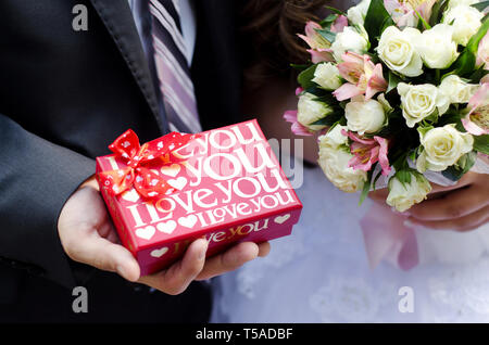 La boîte rouge avec amour dans les mains de la mariée et le bouquet dans les mains de la mariée libre Banque D'Images