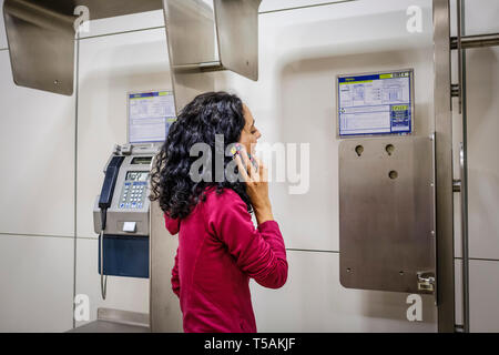 Femme blanche avec des cheveux noirs à l'aide d'un téléphone portable à côté d'une cabine téléphonique publique Banque D'Images