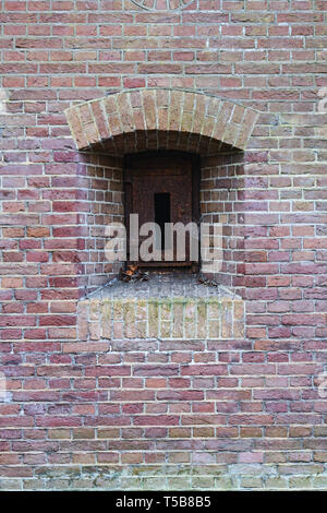 Mur de briques d'une ancienne forteresse avec un embresures fermé avec un fer rouillé berline. Banque D'Images