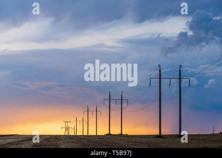 Paysage rural avec la ligne haute tension sur le coucher du soleil. Vue du ciel dramatique Banque D'Images