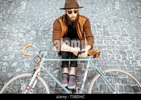 Portrait d'un hipster barbu habillé élégamment avec chapeau brun et l'homme assis avec retro location sur une rue de la chaussée Banque D'Images