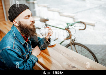 L'homme élégant bénéficiant d''un verre de café alors qu'il était assis au café près de la fenêtre avec retro location en plein air Banque D'Images
