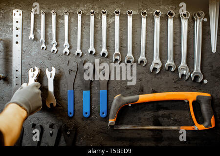 L'homme en tenant le mur noir de clés avec différents outils pour la réparation de vélos Banque D'Images