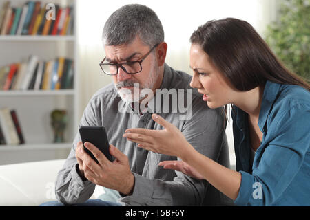 Père et fille confus essayant d'utiliser un téléphone intelligent assis sur un canapé à la maison Banque D'Images