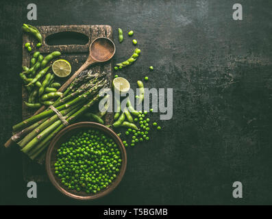 Les asperges vertes avec le soja Edamame, la chaux et les pois verts sur fond noir table de cuisine rustique, vue du dessus. Copier l'espace. L'alimentation végétarienne saine . Gr Banque D'Images