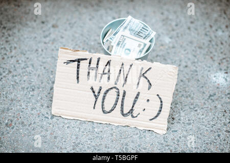 Beggar's cup avec de l'argent et le carton avec message de remerciement sur rue Banque D'Images