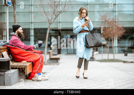 Les sans-abri de l'argent en mendiant assis sur le banc avec passant par businesswoman près du centre d'affaires Banque D'Images