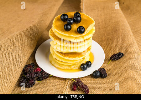 Pile de crêpes faites maison frshed avec miel et bleuets dans une plaque blanche avec des tas de sacs Mulberry Banque D'Images