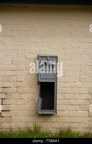 Une boîte victorienne avec son manque de porte, peint en gris pâle sur un mur de briques, avec l'herbe pousse à la base. Orientation portrait Banque D'Images