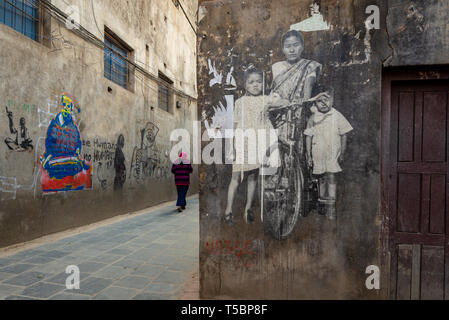 Kathmandu, Patan, NÉPAL - 3 avril 2019 : une femme népalaise à monter une ruelle étroite et en passant en face de peintures murales et graffitis de rue Banque D'Images