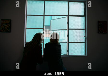 Silhouette of woman and girl looking out window de verre dépoli, fenêtre turquoise. Banque D'Images