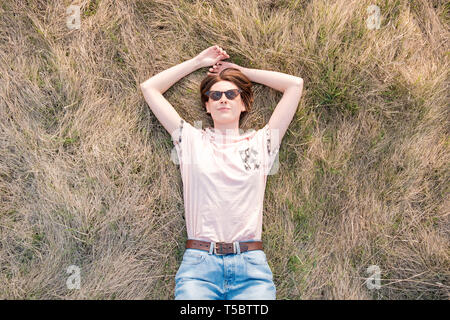 Jeune femme sur l'herbe profitant du printemps. Vue de dessus d'une personne de sexe féminin dans le pré de pose ou un champ de regarder le ciel Banque D'Images