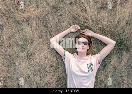 Jeune femme repose sur l'herbe profitant du printemps. Vue de dessus d'une personne de sexe féminin dans le pré de pose ou un champ de regarder le ciel, de copie savs Banque D'Images