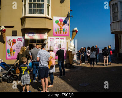 Les touristes et vacanciers formant une file d'attente ordonnée pour acheter des glaces traditionnelles à partir d'un vendeur de crème glacée, le long de la rue dans le centre-ville de Cromer Banque D'Images