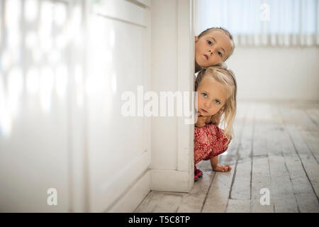 Deux jeunes soeurs blonde peek autour du bord d'une porte. Banque D'Images