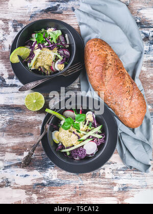 Vue supérieure de la ciabatta italien salade de légumes frais et sombre dans un bol. Avec salade de radis, chou rouge, concombre, le pesto et les graines de sésame. Banque D'Images