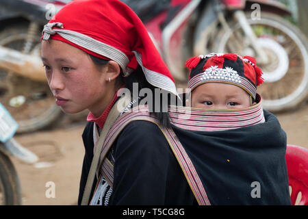 TA PHIN, LAO CAI, VIETNAM - 12 janvier 2019 : un petit enfant dans un sac derrière une adolescente. Dzao rouge - une petite nation du Nord Vietnam Banque D'Images