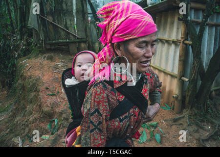 TA PHIN, LAO CAI, VIETNAM - 12 janvier 2019 : un petit enfant dans un sac derrière une mère. Dzao rouge - une petite nation du Nord Vietnam Banque D'Images